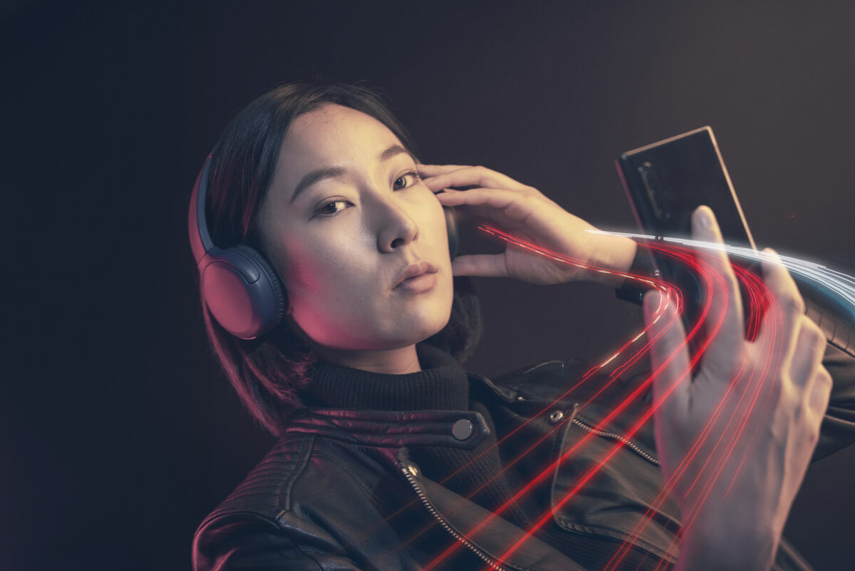 A woman wearing wireless headphones, holding her smartphone.