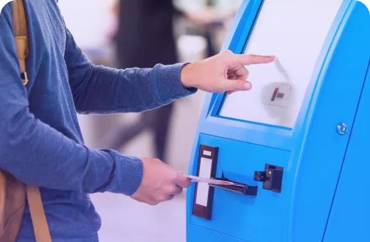 Traveller collecting a printed ticket from a blue self-service ticket kiosk.
