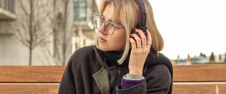 Young woman wearing headphones, enjoying music outdoors, with a vibrant purple background.