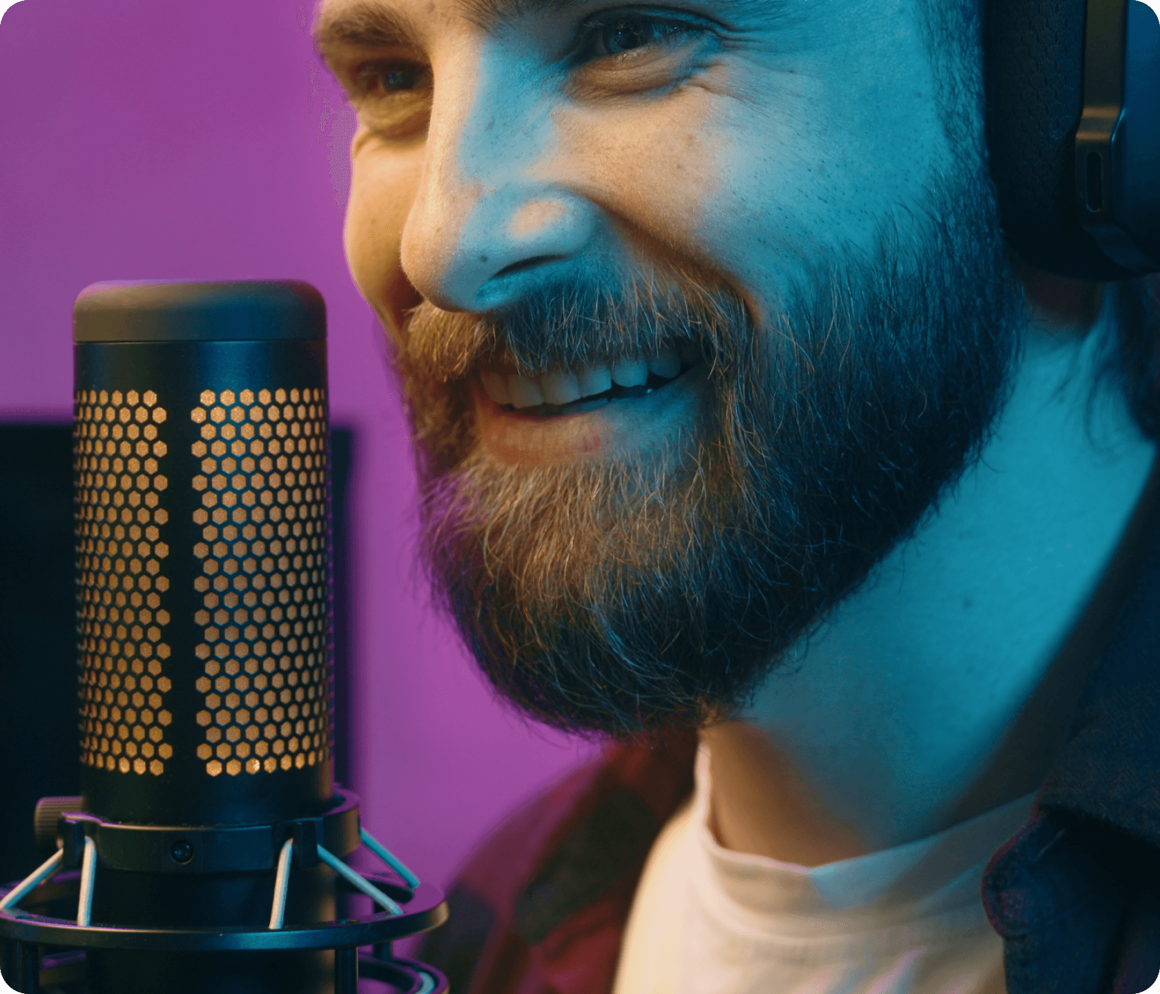 Smiling man in headphones speaking into a microphone with colorful lighting background.