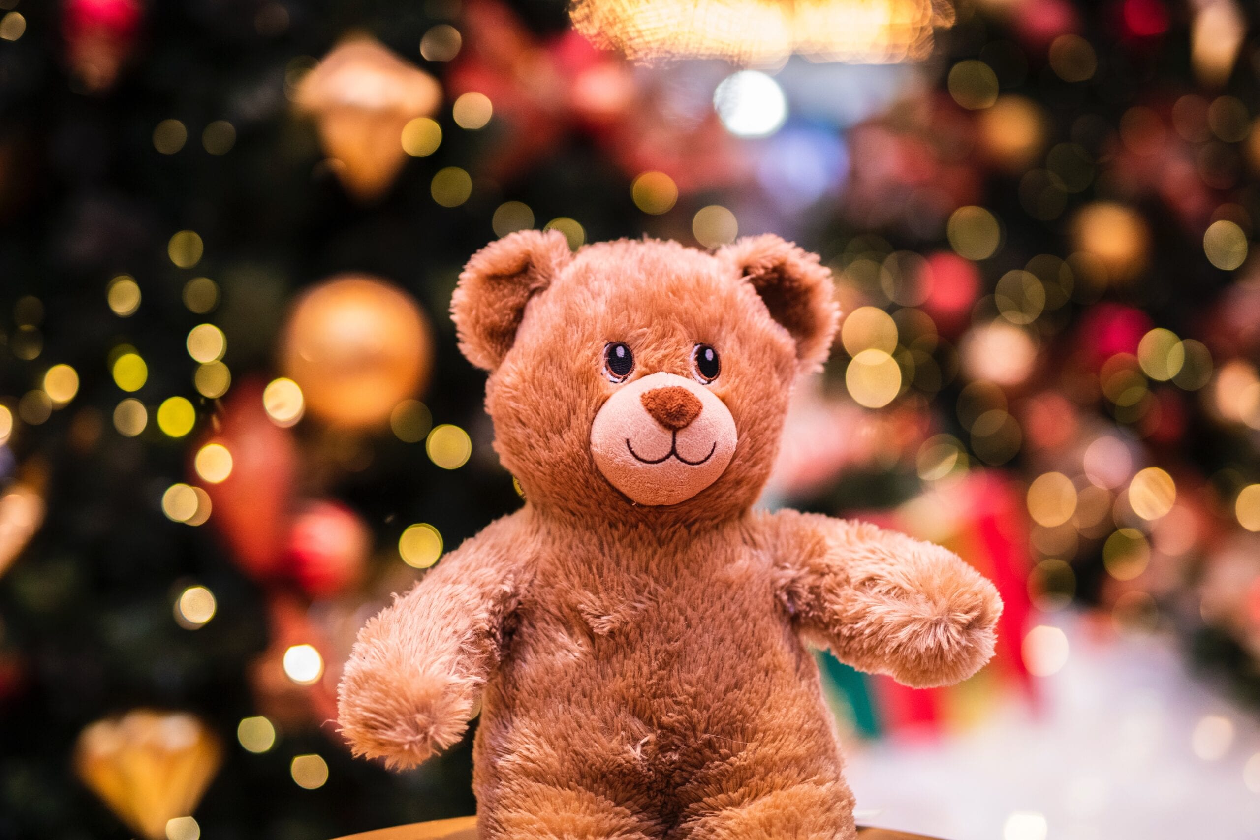 A plush teddy bear in front of festive lights