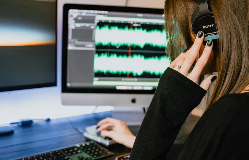 Eine Frau hört über Kopfhörer am Computer zu.