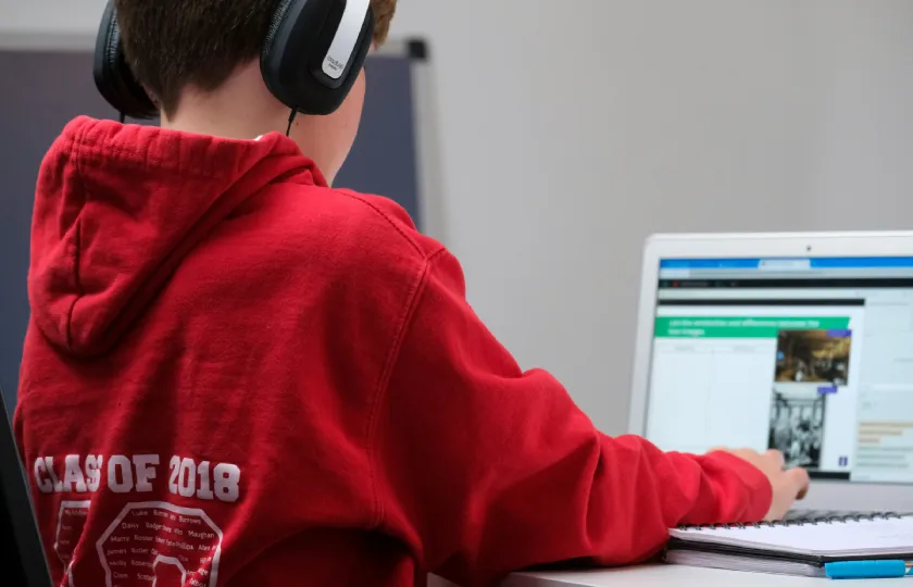 Un étudiant porte un casque audio tout en utilisant un ordinateur portable assis à un bureau.