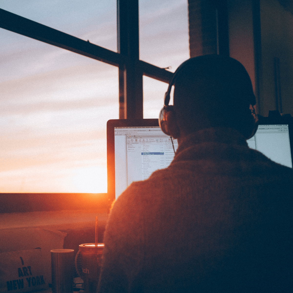 A learner with headphones studying at a computer by a window at sunset