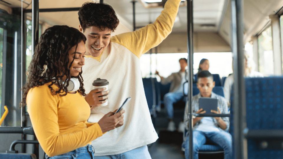 Duas pessoas observam um smartphone em um ônibus.