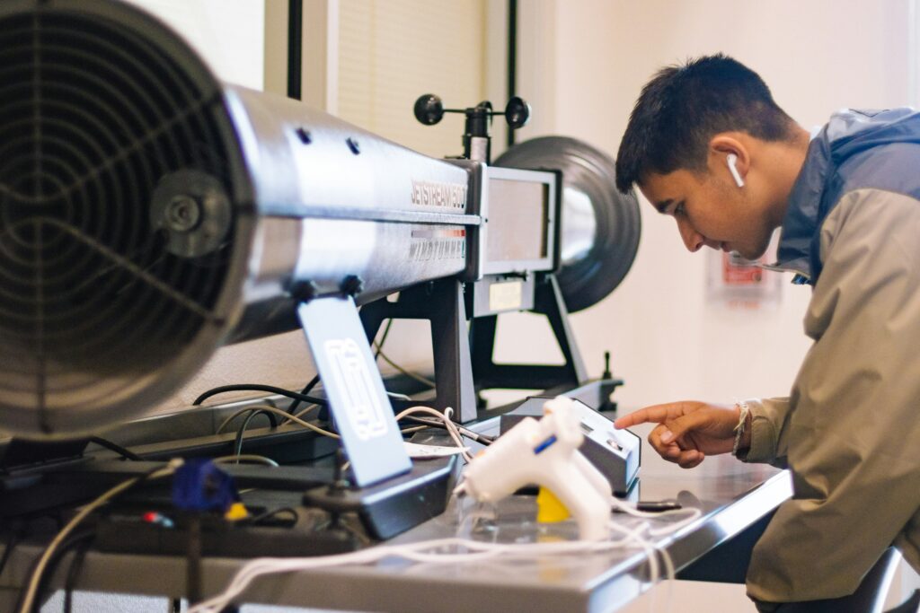 Junger Auszubildender mit Kopfhörern arbeitet an der Mechanik einer Windturbine auf dem Tisch vor ihm.