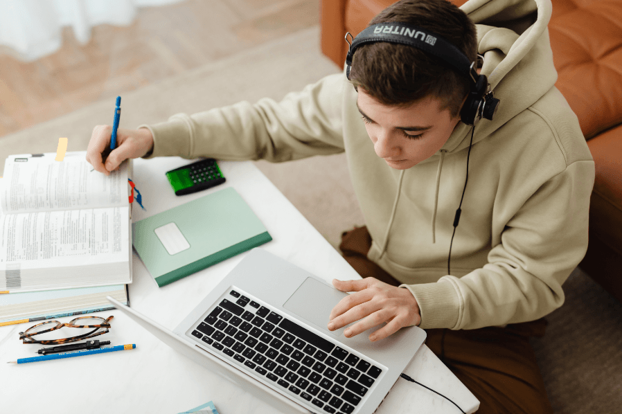 Étudiant assis à un bureau utilisant un ordinateur portable et un casque pour un apprentissage accessible..