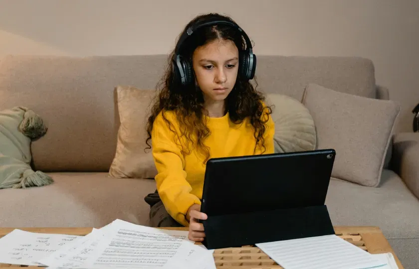 Une étudiante portant un casque audio regarde une tablette posée sur une table basse.