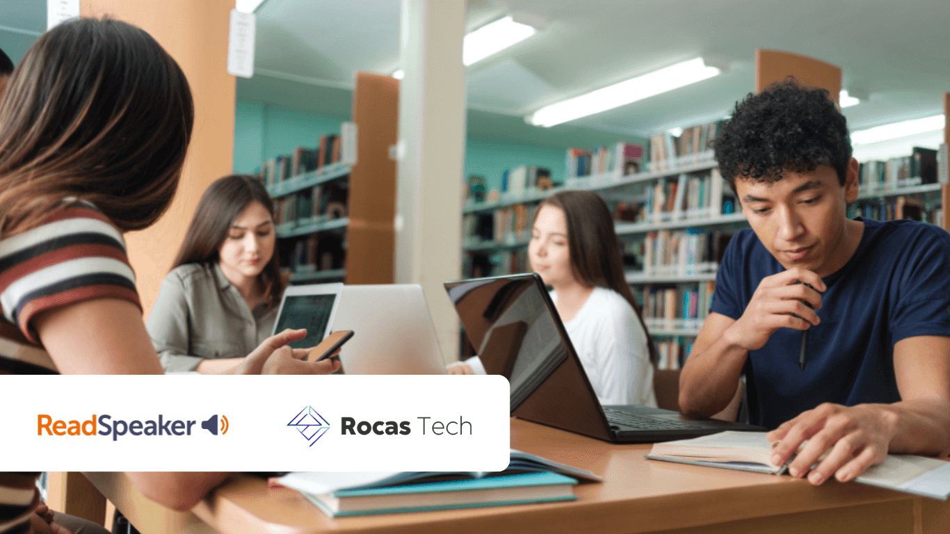 Alunos sentados à mesa em uma biblioteca, aprendendo com livros, laptops e celulares.