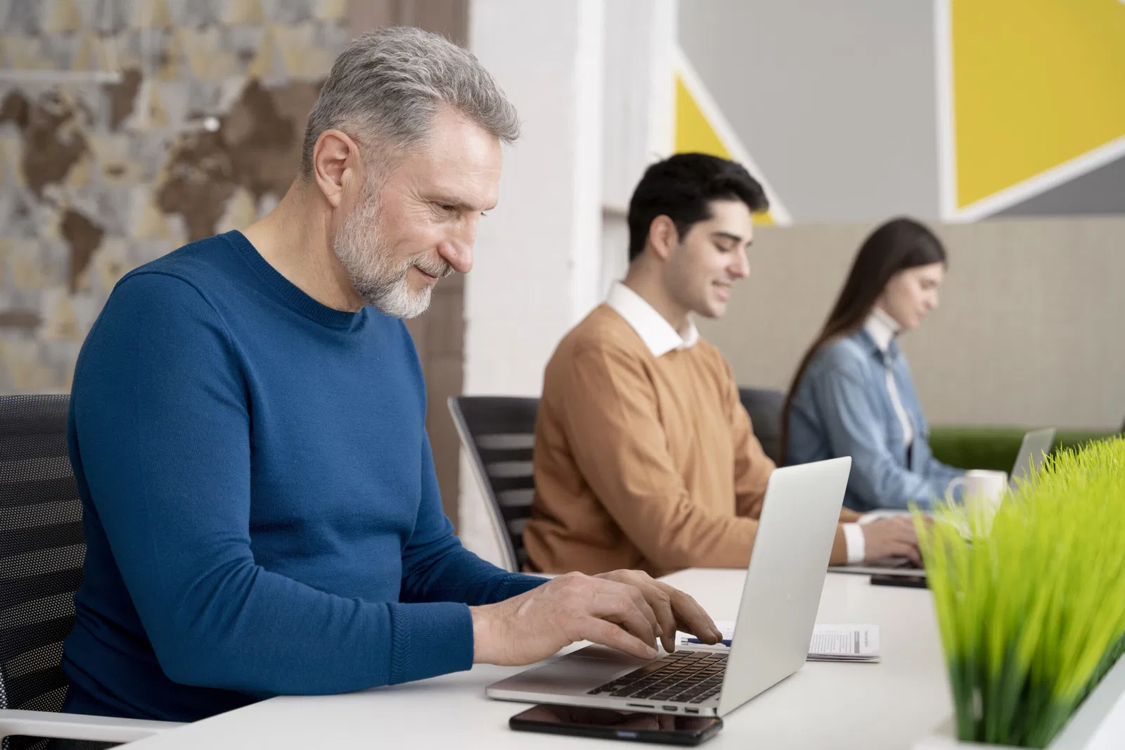 Três pessoas estão em frente aos seus laptops.
