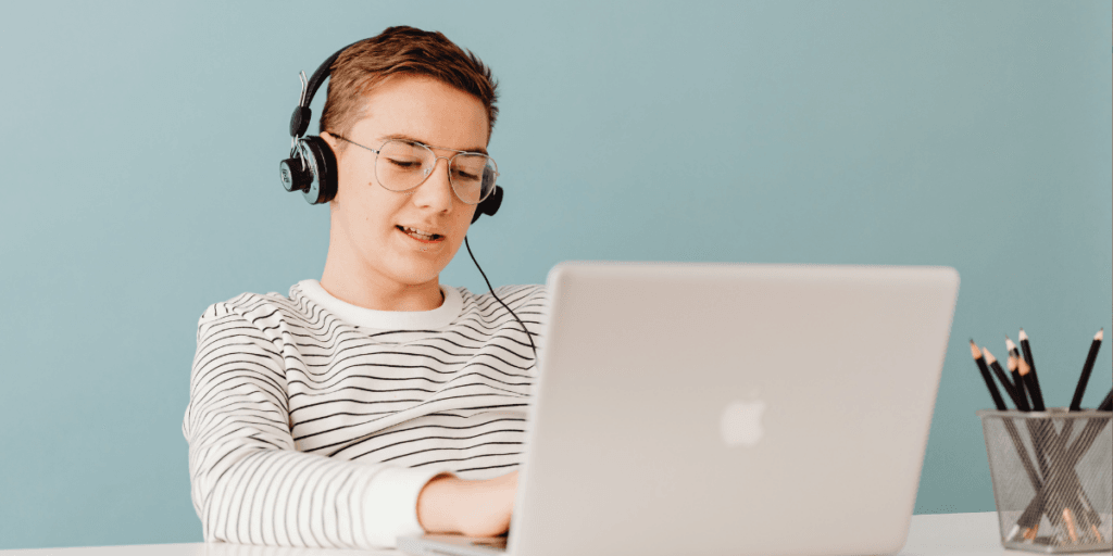 Image d’un jeune homme portant un t-shirt rayé blanc et noir, assis à un bureau, travaillant sur un ordinateur portable et portant un casque.