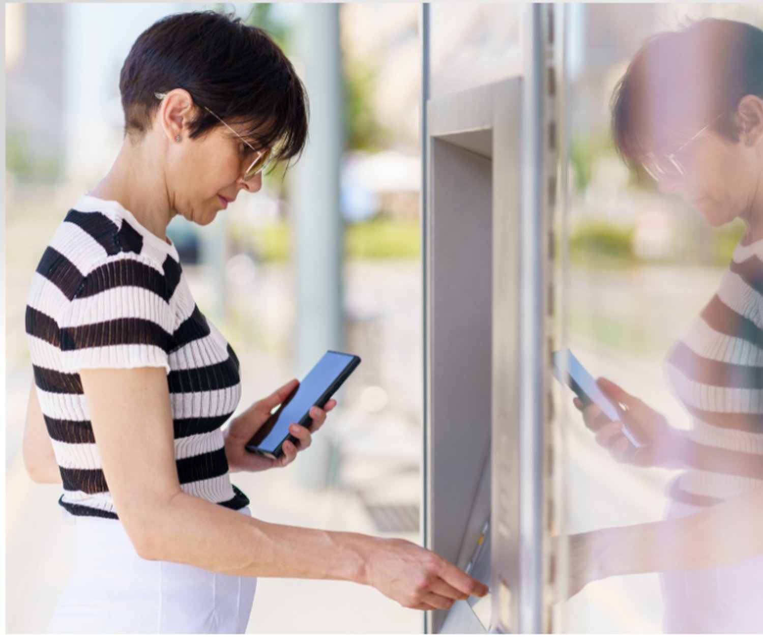 Persona che utilizza un terminale self-service digitale e uno smartphone in un ambiente pubblico, illustrando servizi digitali accessibili e sistemi self-service inclusivi.