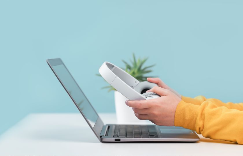 E-learner zit achter laptop met koptelefoon in de hand.